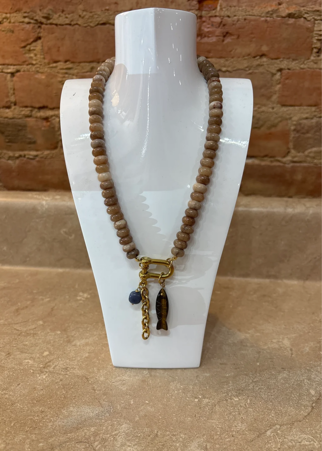 Brown beaded necklace with charms on a white display with a brick background.