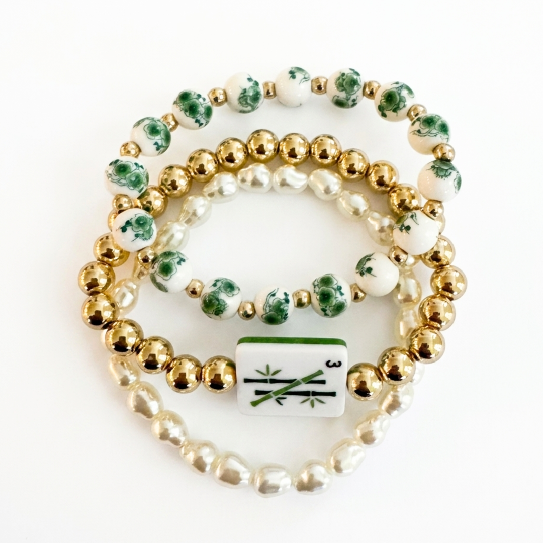 Set of three beaded bracelets with gold, green, and white beads on a white background