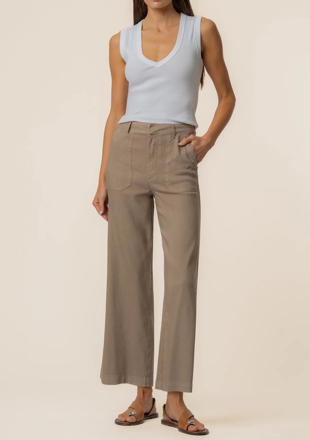Woman wearing a light blue sleeveless top and beige wide-leg pants on a beige background
