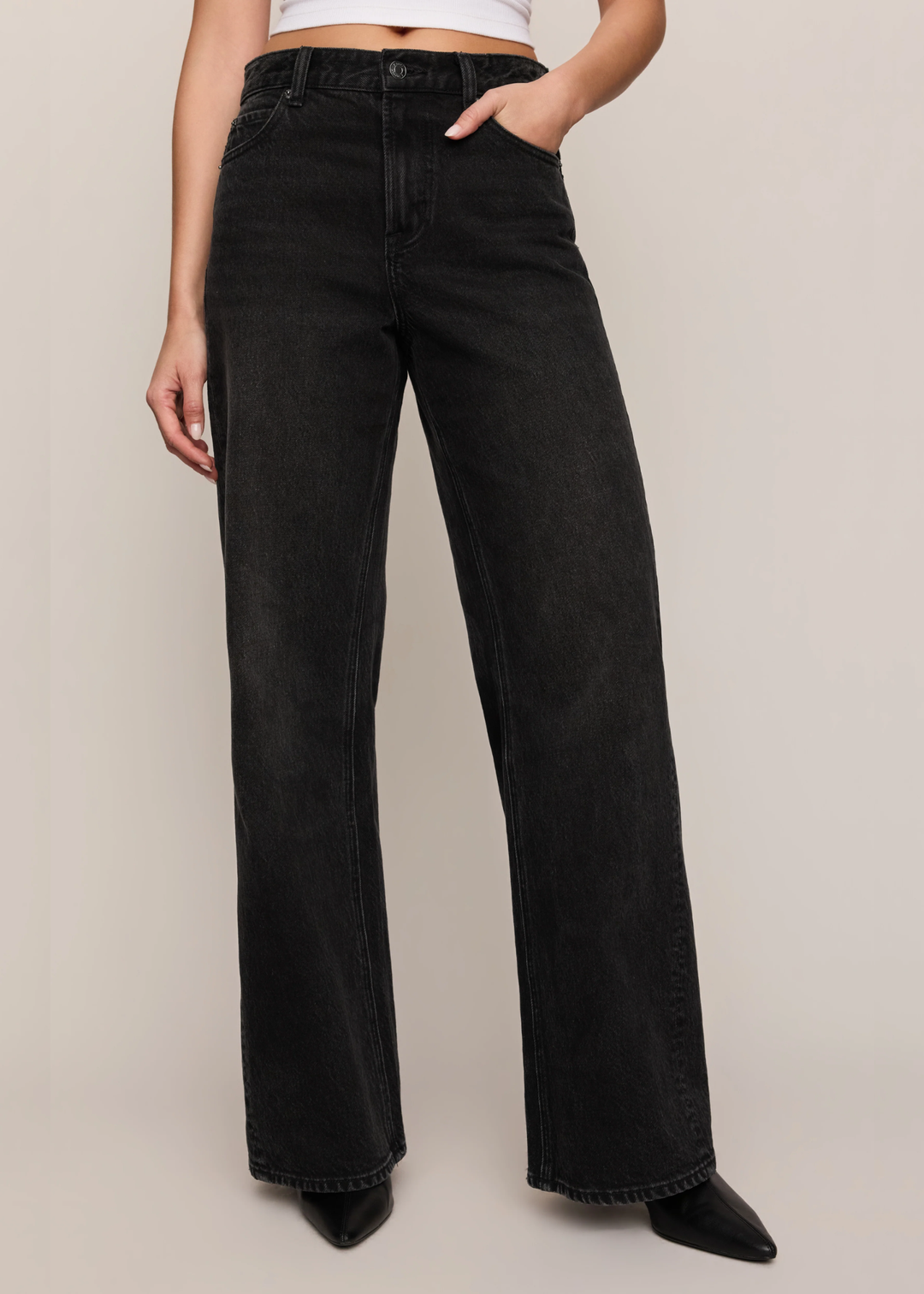 Model wearing black denim with a black boot and hand in the pocket. 