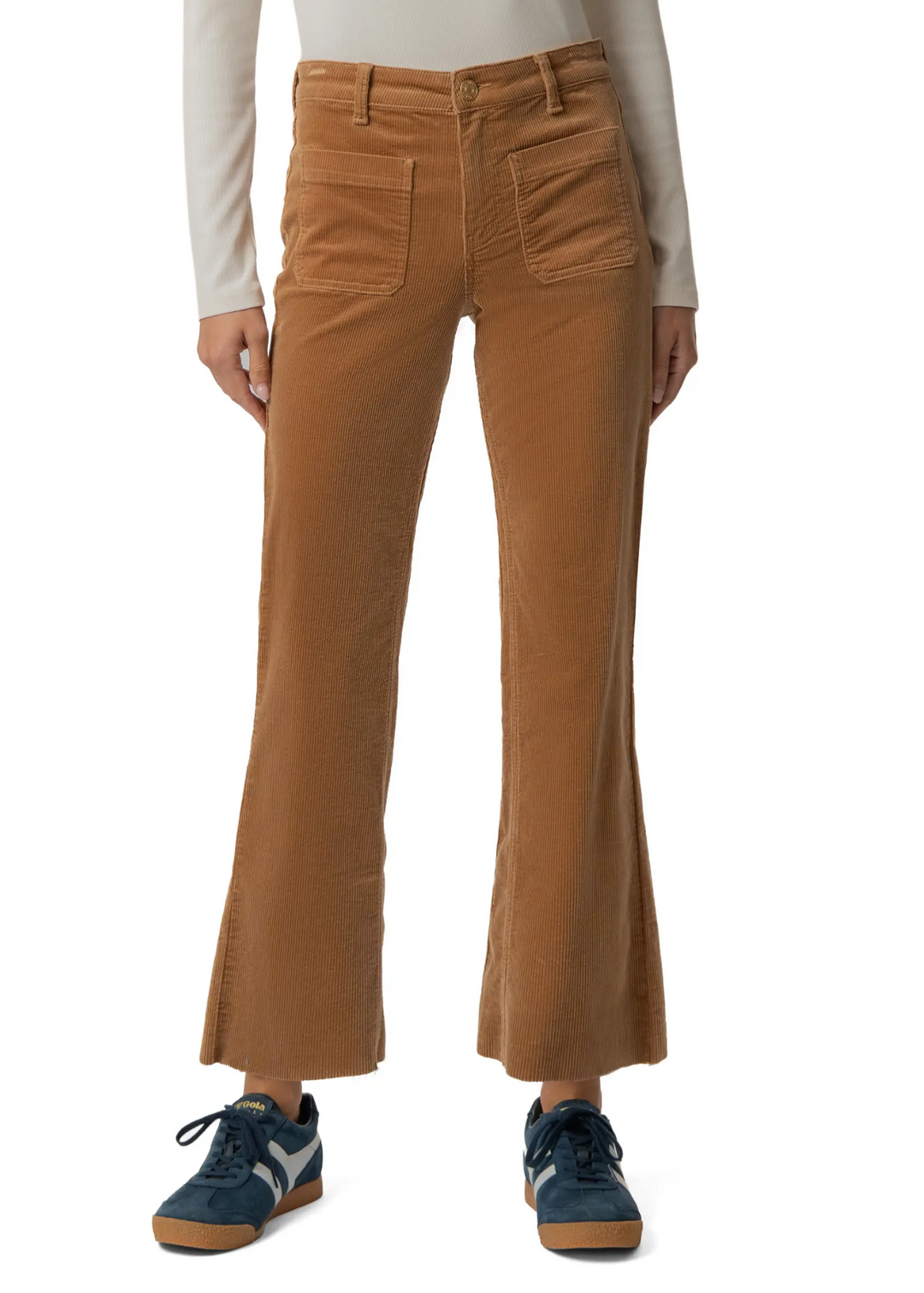 A person wearing tan corduroy flare pants with a cream long-sleeve top and blue sneakers, shown from the waist down on a white studio background.