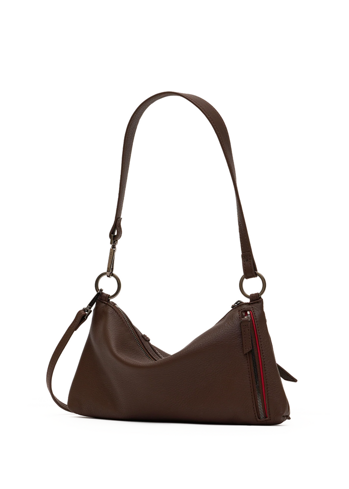 A dark brown pebbled leather shoulder bag with a crescent shape, featuring a long adjustable strap, metal hardware, and a vertical red accent zipper pull on the front.