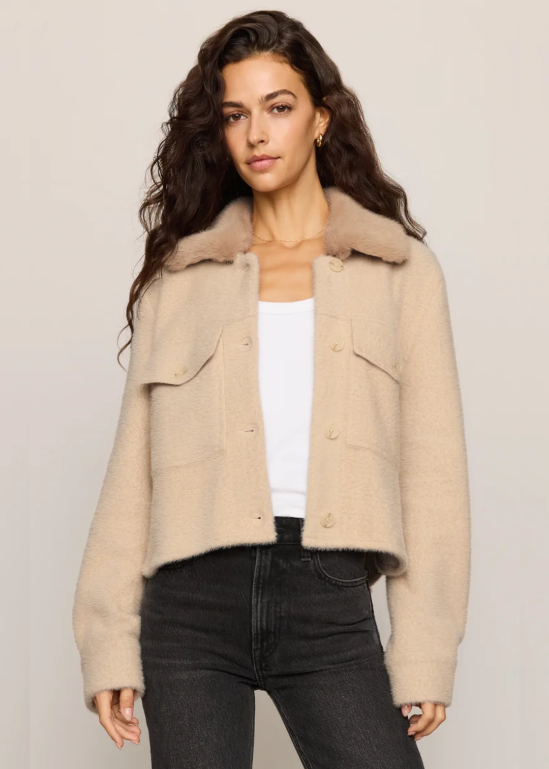 Woman wearing tan fuzzy jacket open with a white tank underneath. 