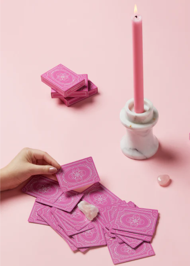 Someone holding a pink card with pink cards, a candle, and pink card boxes surround