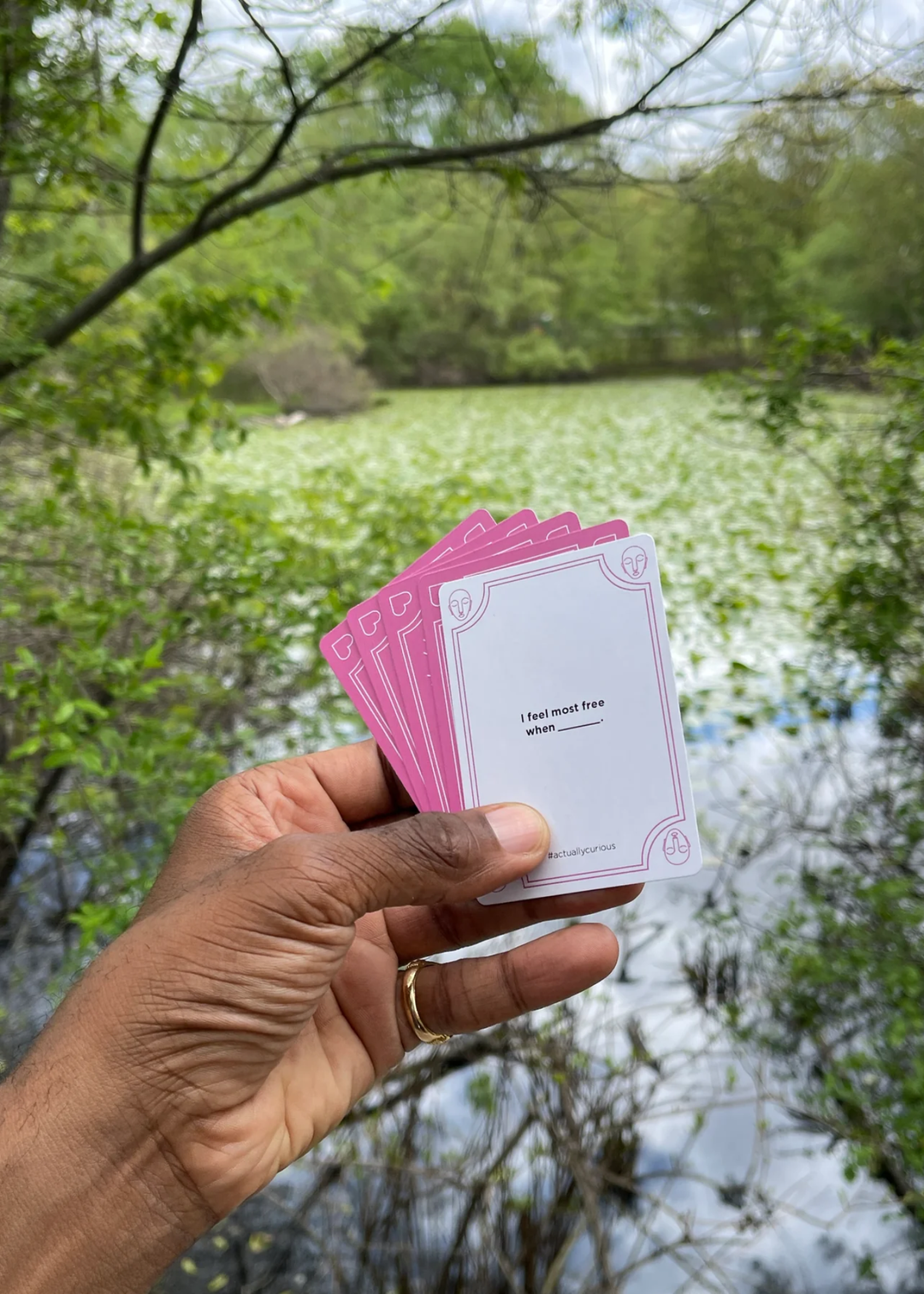 A person holding pink cards and a white card with a question in front of a lake