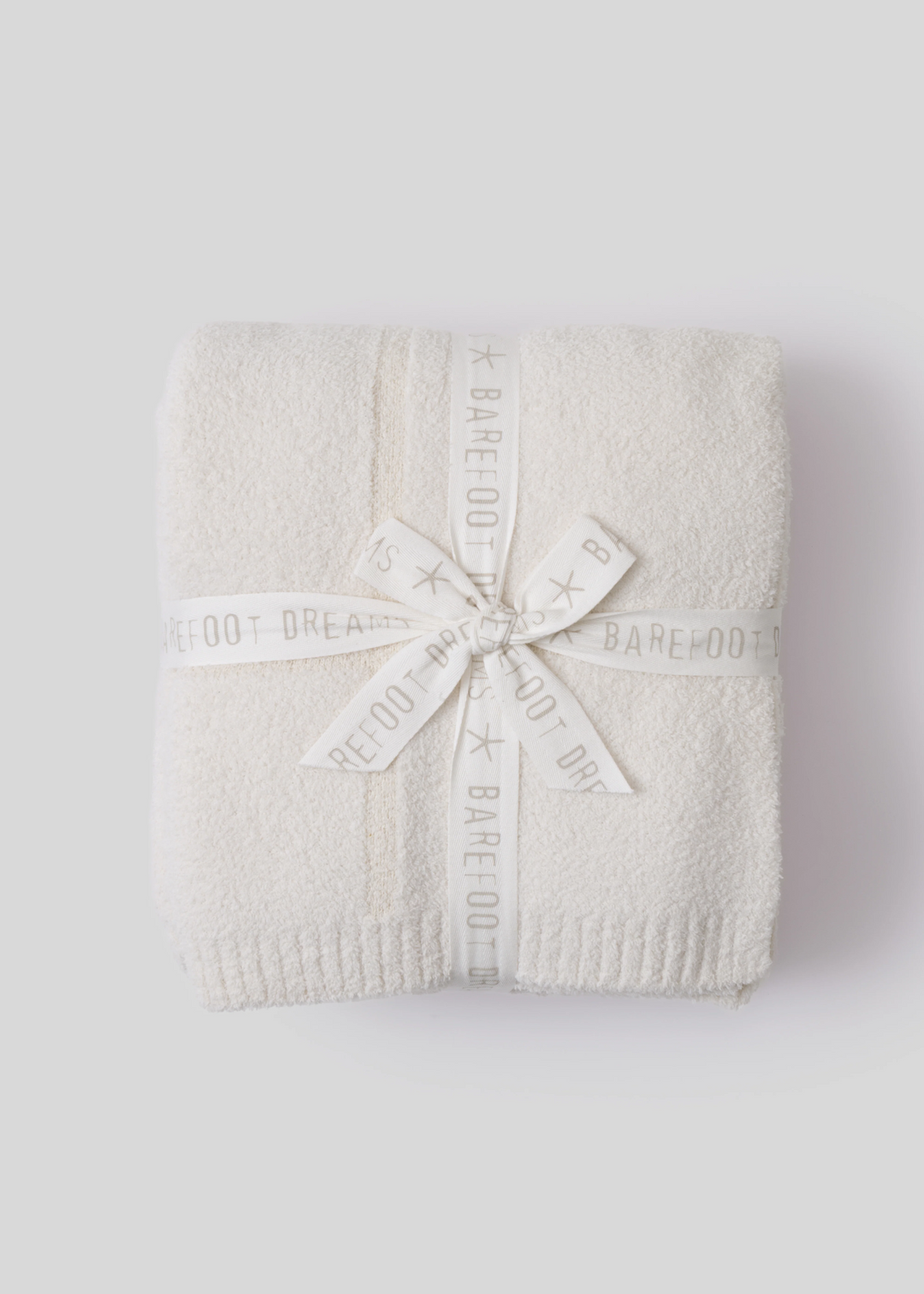 Cream colored blanket folded and tied with white ribbon sitting on a white background