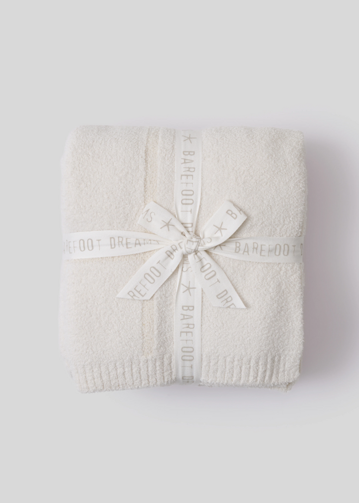 Cream colored blanket folded and tied with white ribbon sitting on a white background