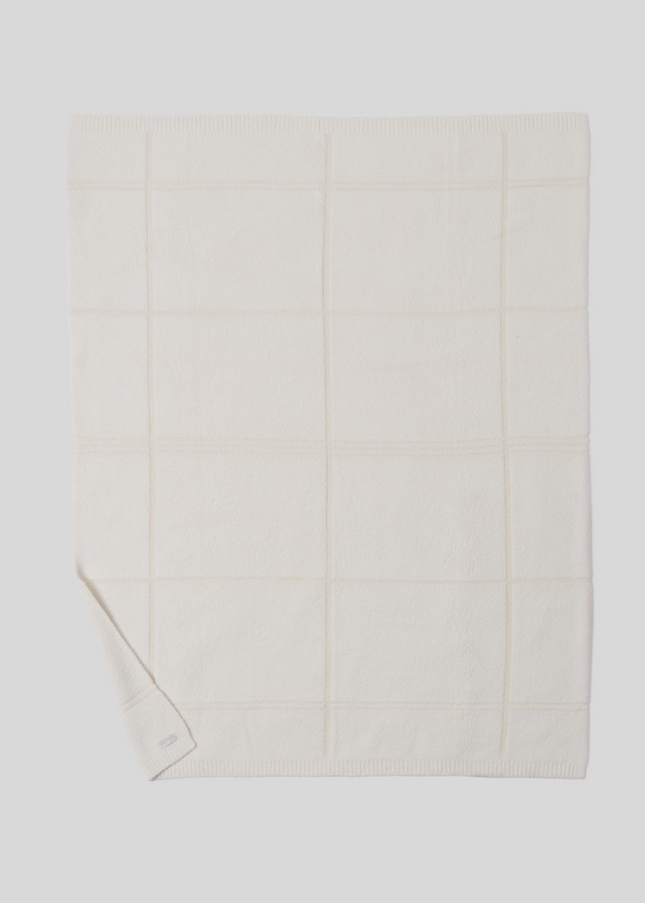 Cream colored plaid blanket layed out on a white background with a lower corned folded