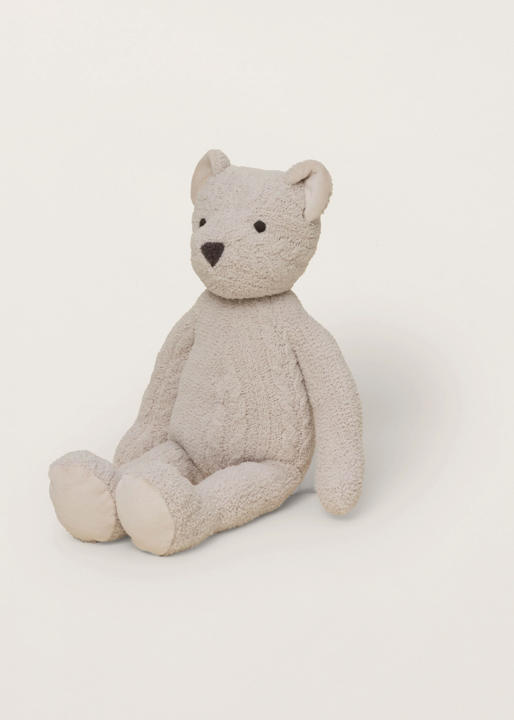 Tan stuffed teddy bear sitting on a white background facing the side