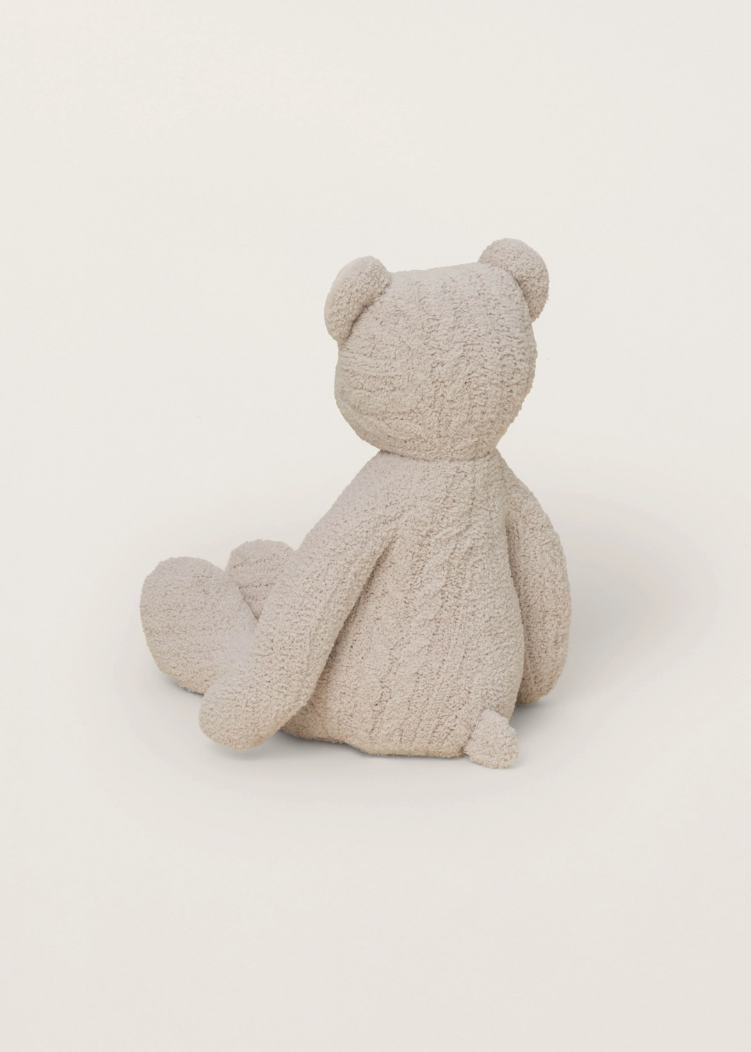 Tan stuffed teddy bear facing backwards sitting on a white background