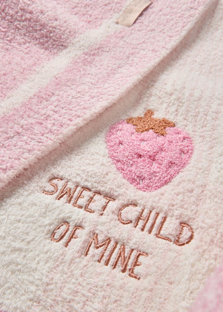 Close up of a pink blanket with a plaid pattern with and embroidered strawberry and "SWEET CHILD OF MINE" lettering