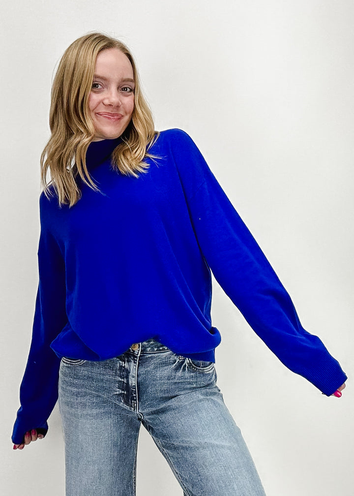 A woman wearing a bright blue oversized long sleeve turtleneck sweater styled with light-wash jeans, creating a cozy and stylish look perfect for fall or winter fashion.