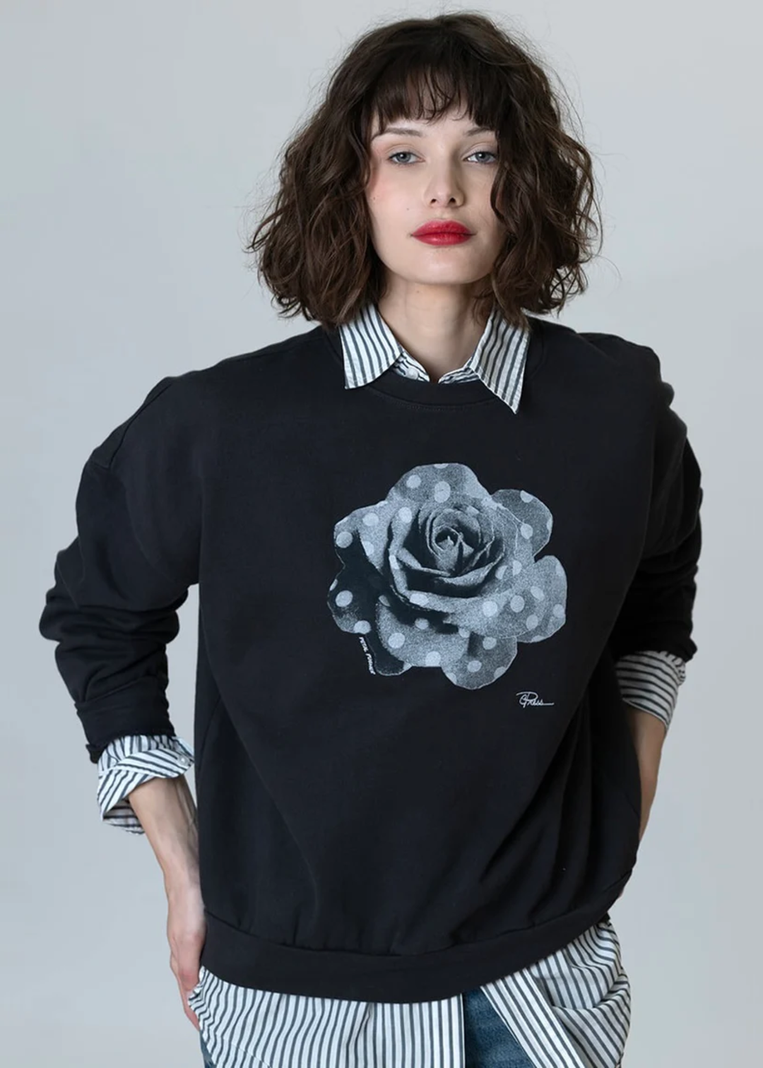 Woman wearing a black sweatshirt with a black and white polka dot rose graphic over a black and white striped button down