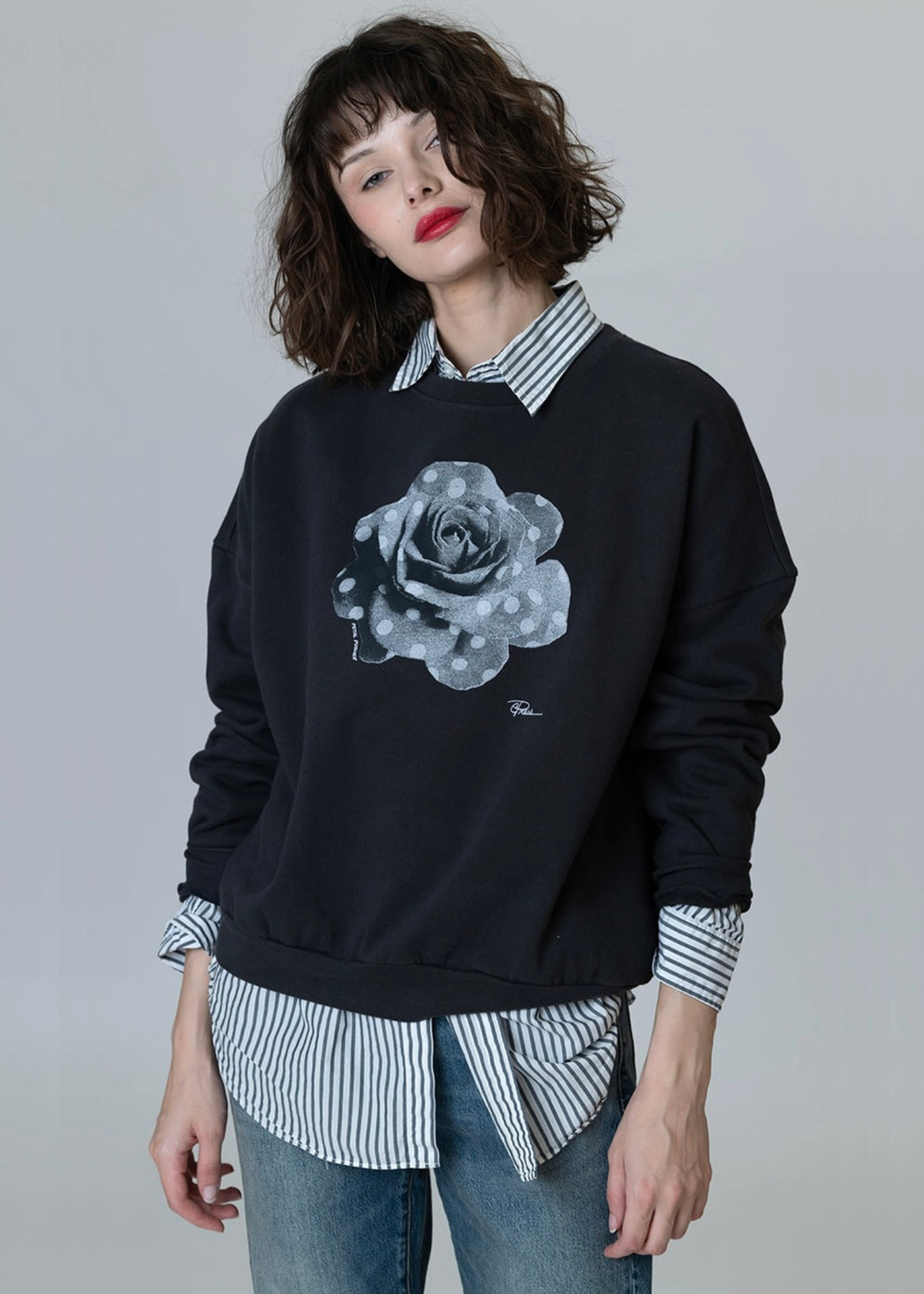 Woman wearing a black sweatshirt with a black and white polka dot rose graphic over a black and white striped button down