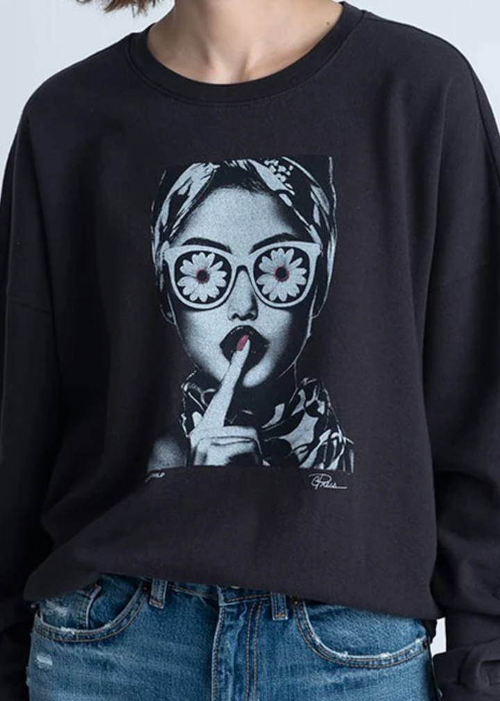 Woman wearing a black sweatshirt with a flower face graphic in front of a grey background