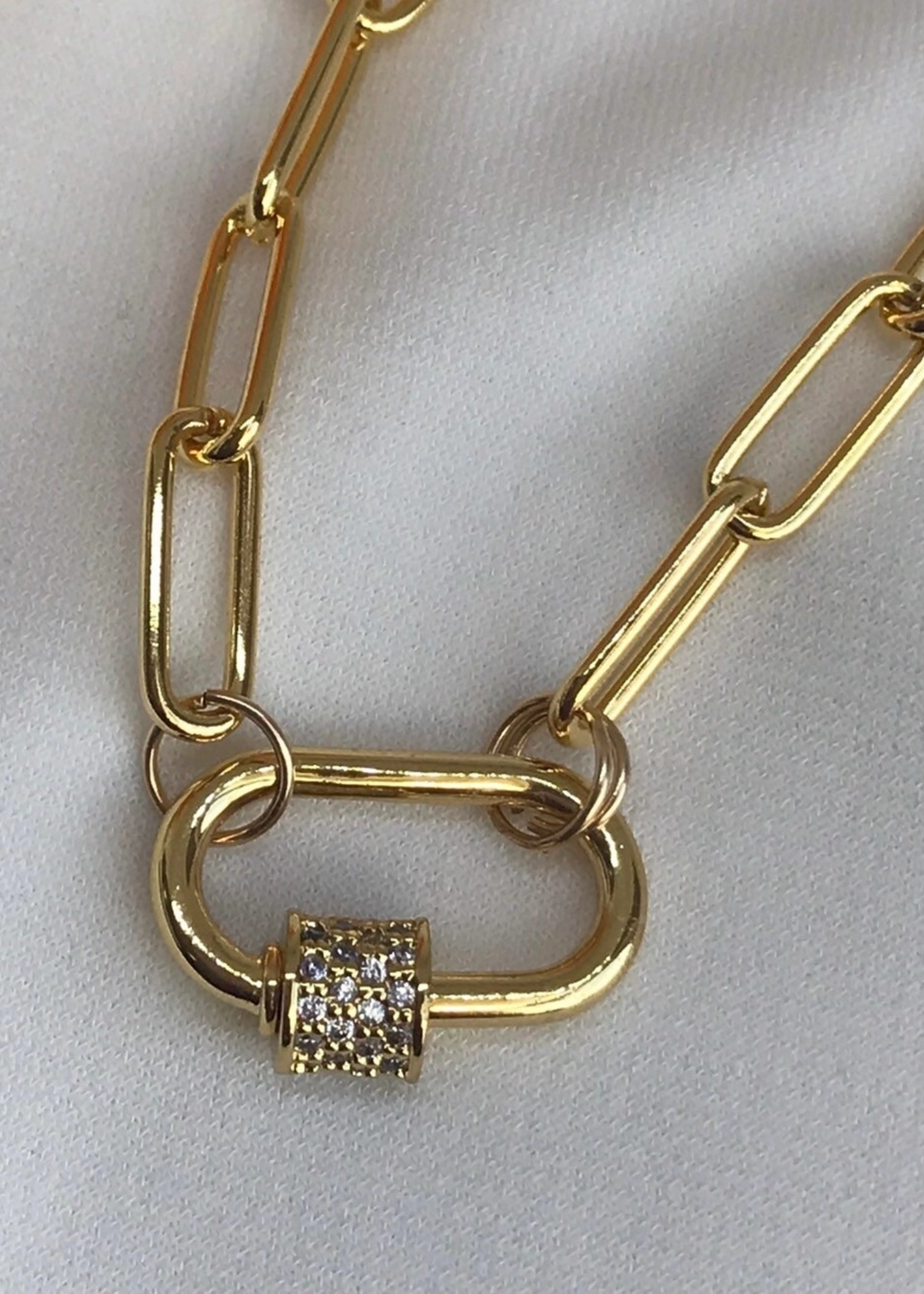Close up of a gold chain necklace with a gold carabiner clasp on a white background