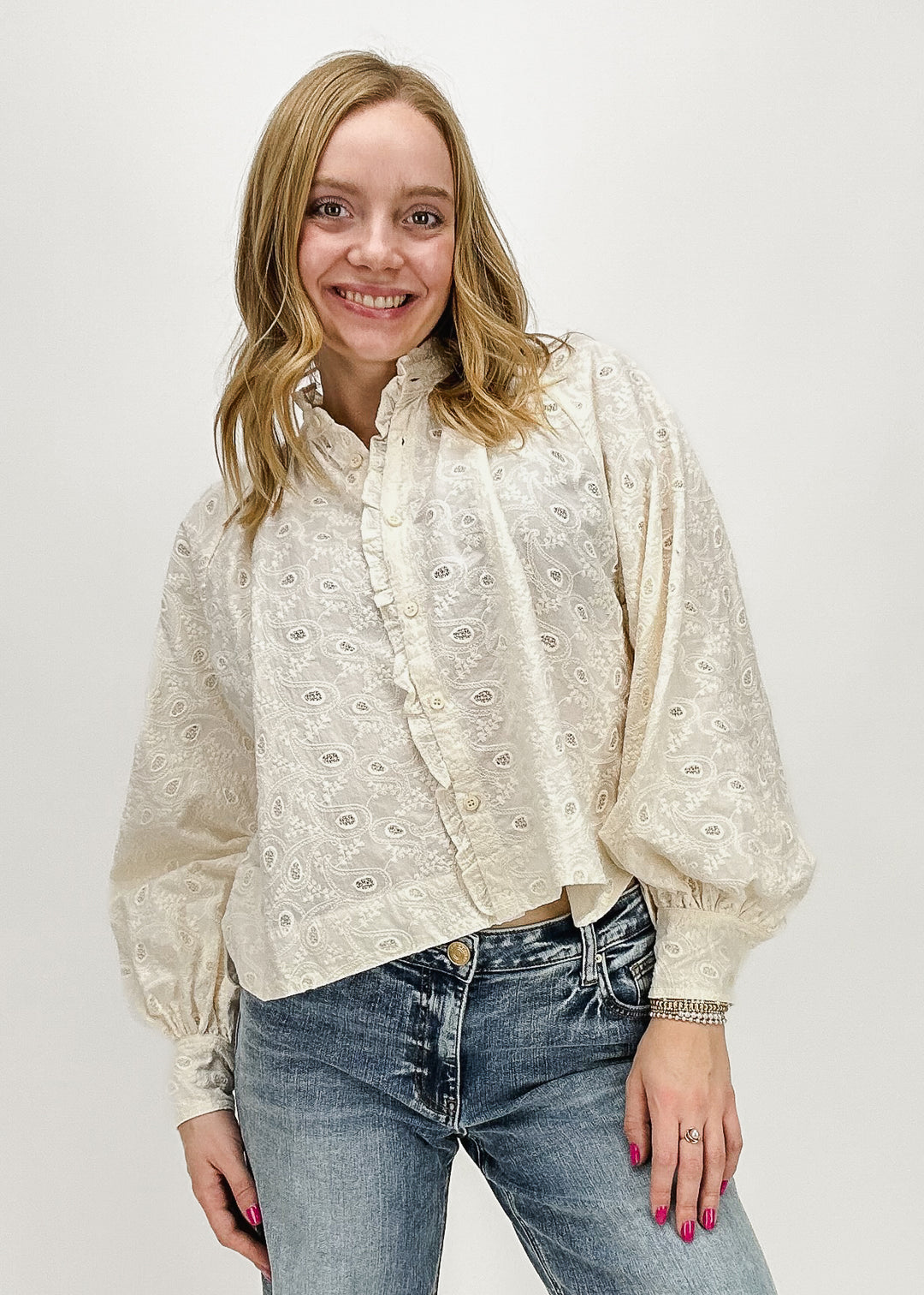 A woman wearing a cream-colored embroidered long-sleeve button-up blouse by FRNCH Paris, styled with light-wash jeans, perfect for an elegant yet casual everyday look.