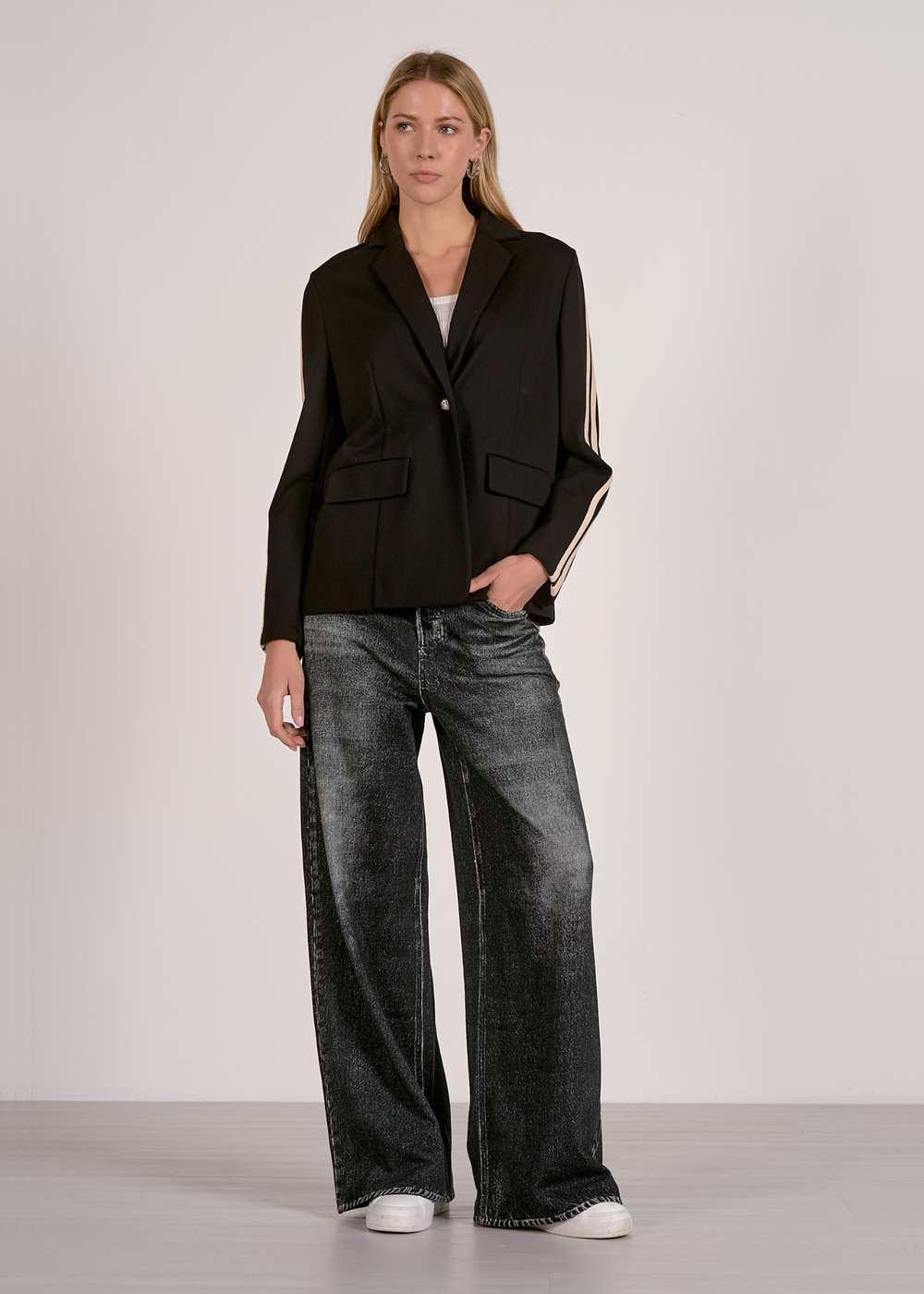 Woman wearing a black blazer with tan sleeve stripes with black washed jeans 