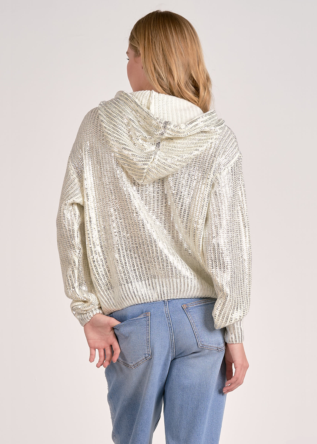 Woman turned around wearing a white sequin hoodie with jeans against a white background