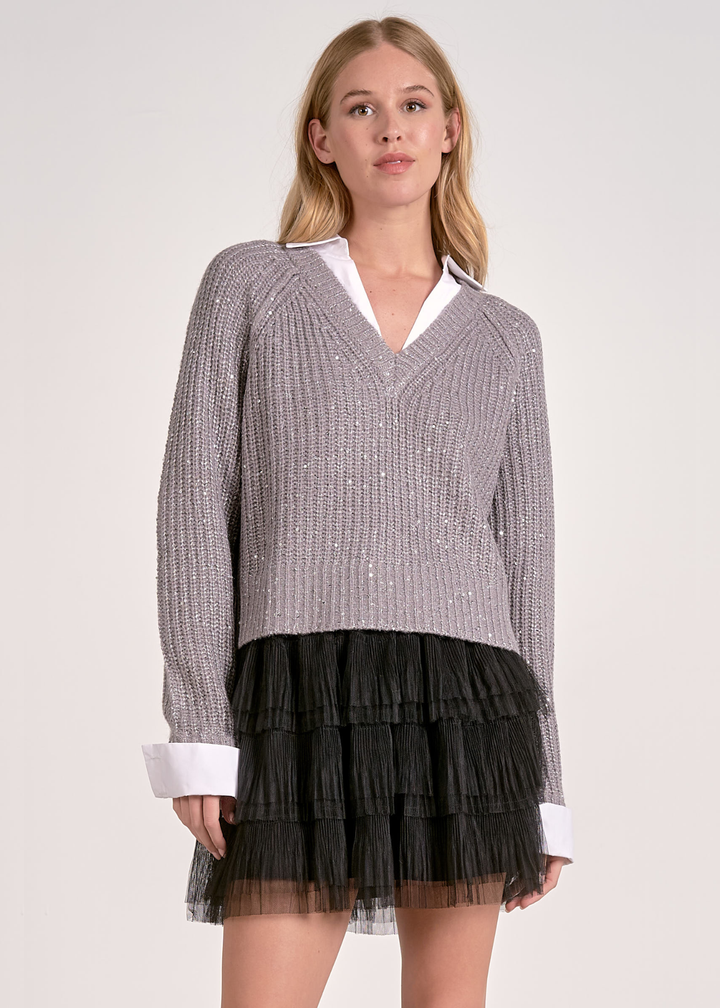 Woman wearing a grey sparkly sweater layered over a white button down with a black mesh skirt