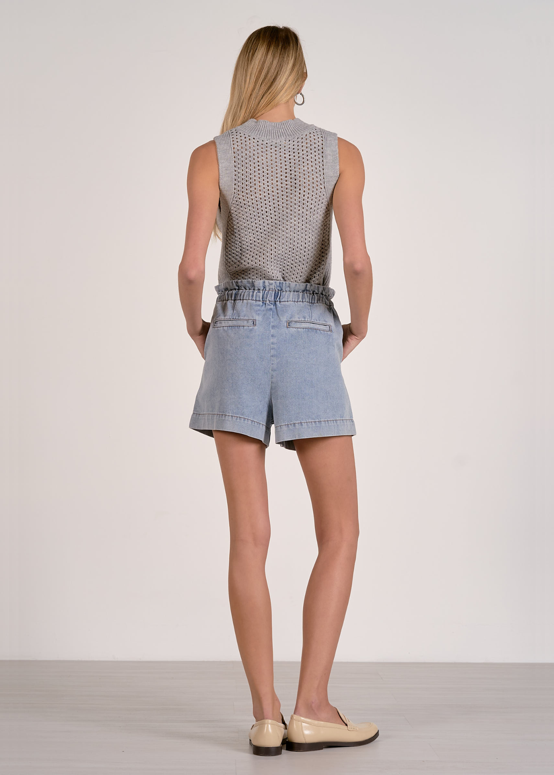 Woman turned around wearing blue shorts with a grey knit tank