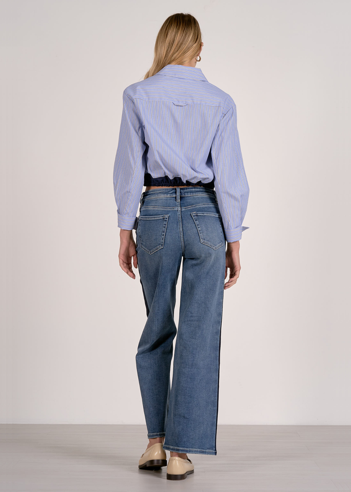 Woman turned around wearing a blue stripe button down with a navy cinched waistline and jeans