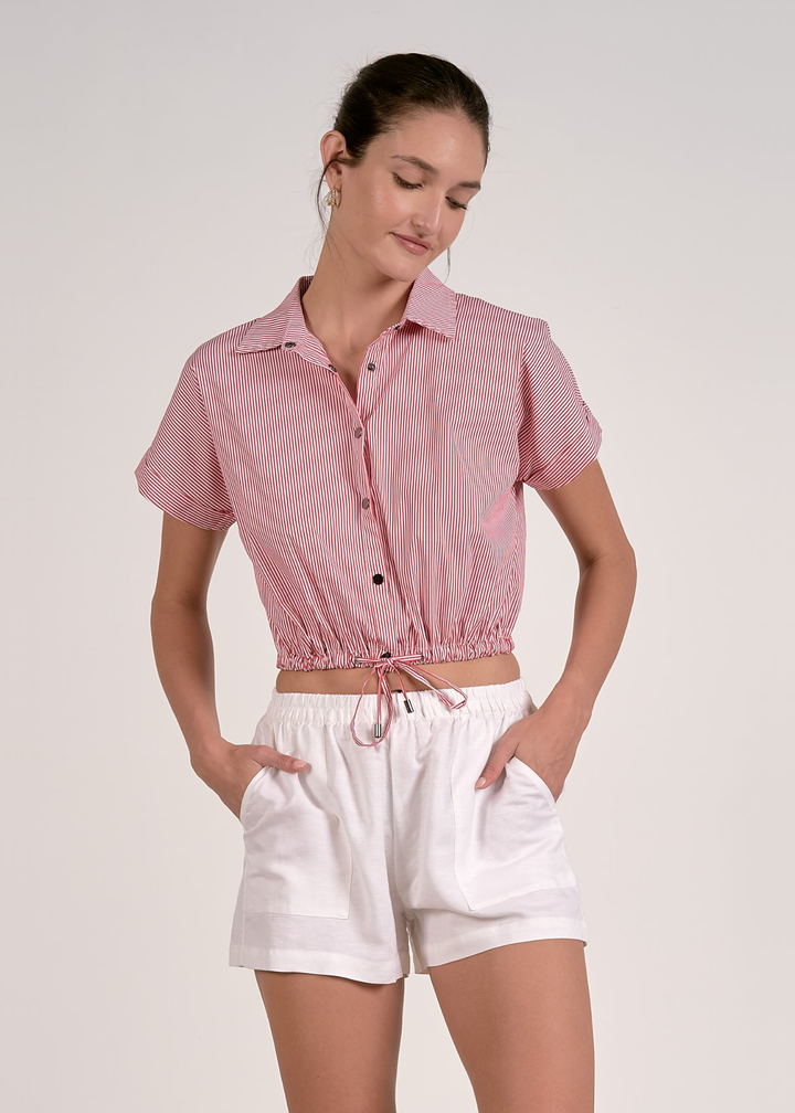 Woman wearing a cropped and short sleeve red and white striped button down with white shorts against a grey background