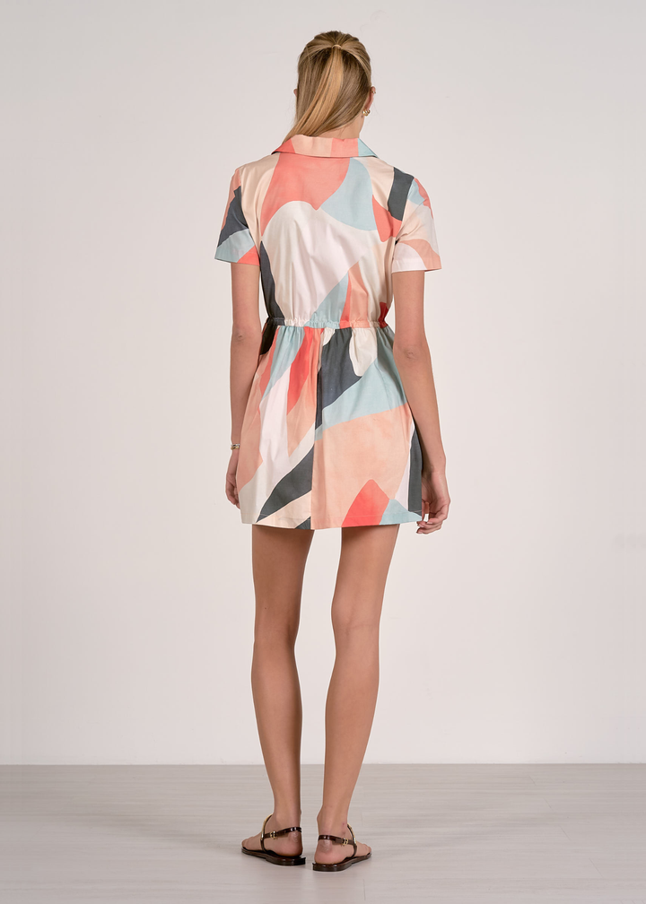 Woman turned around wearing a short sleeve mini dress with a collared neckline and a pastel print pattern