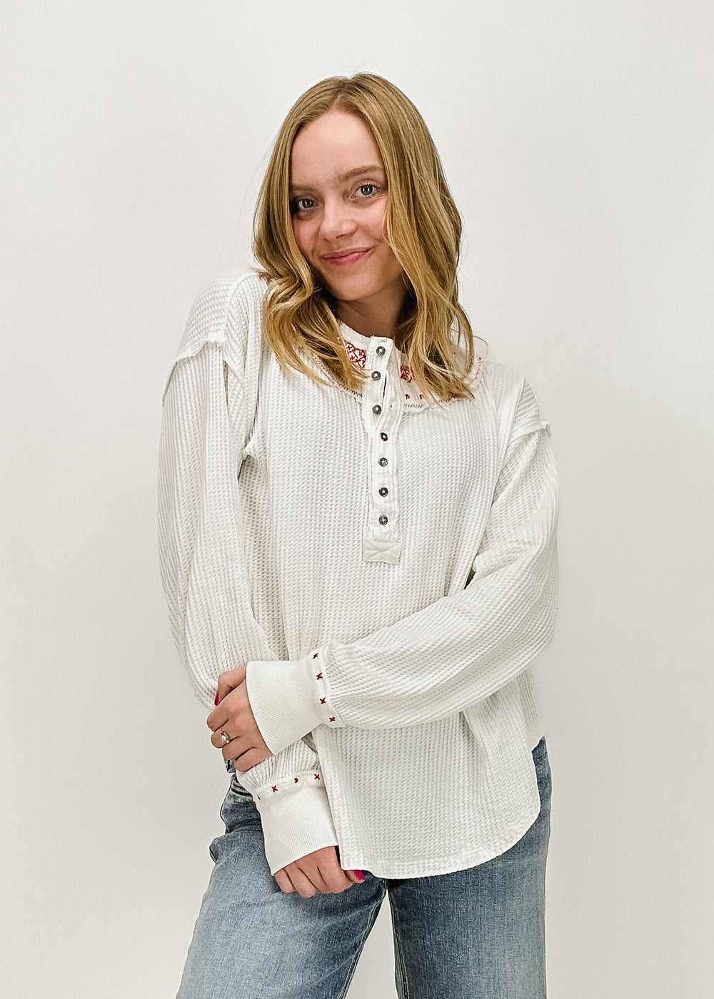 A woman wearing the Free People Holly Henley top in Ivory Combo, a long-sleeve waffle-knit button-up, styled casually with light-wash jeans for a cozy, everyday look