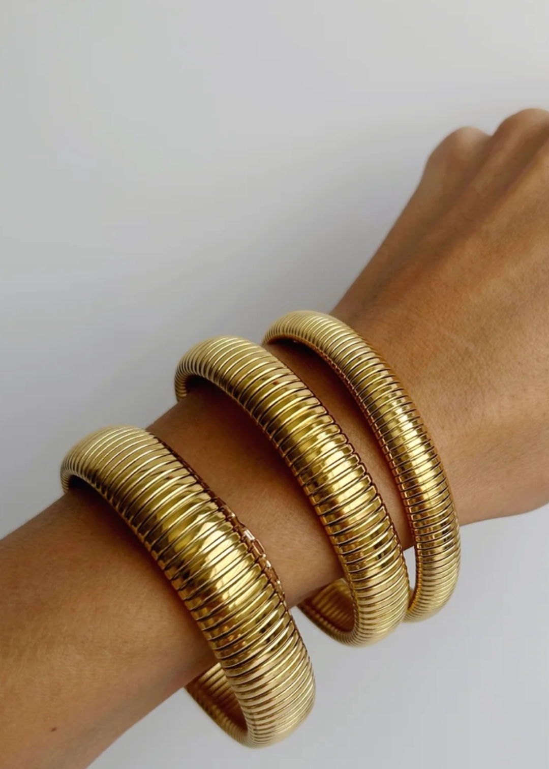 Woman wearing three gold bangle bracelets against a white background