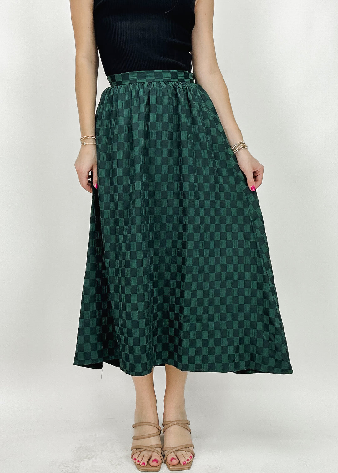 A woman wearing a green checkered A-line midi skirt, styled with a black top, perfect for a classy and elegant everyday look.