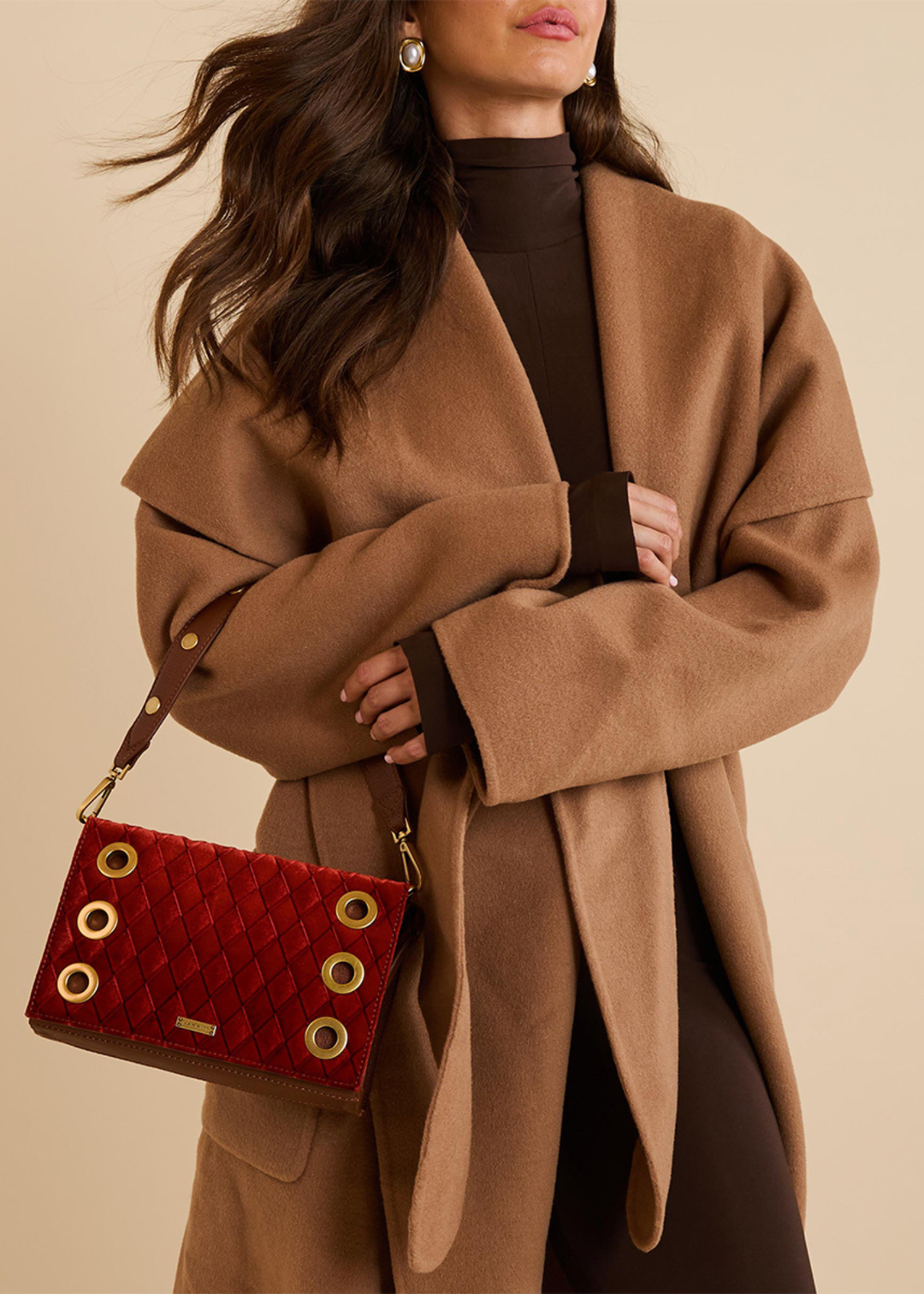 Close up of a woman wearing a brown coat and holding a red velvet and brown leather purse with gold accents