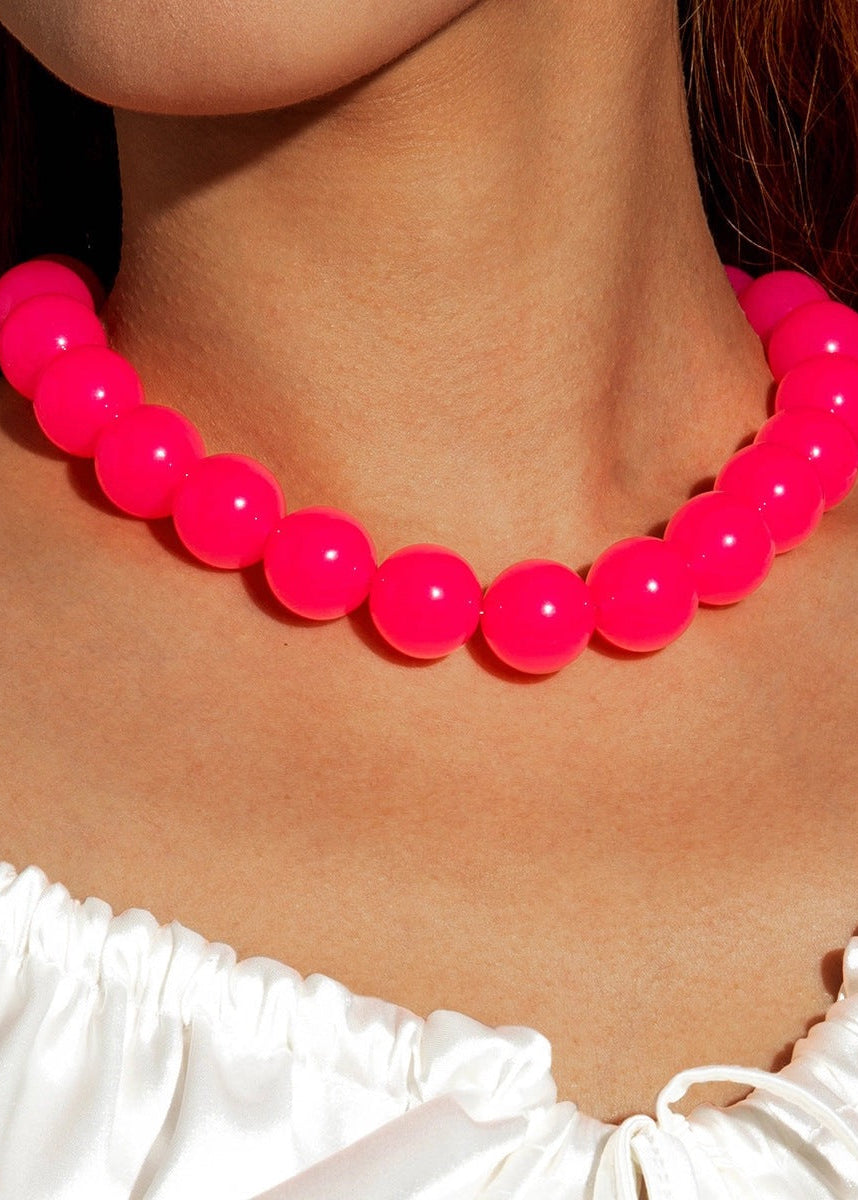 Neon pink beaded necklace worn by a person with a white top.