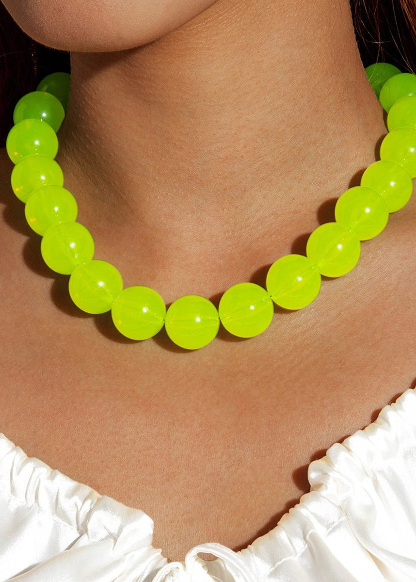 Neon green beaded necklace worn by a person with white ruffled top
