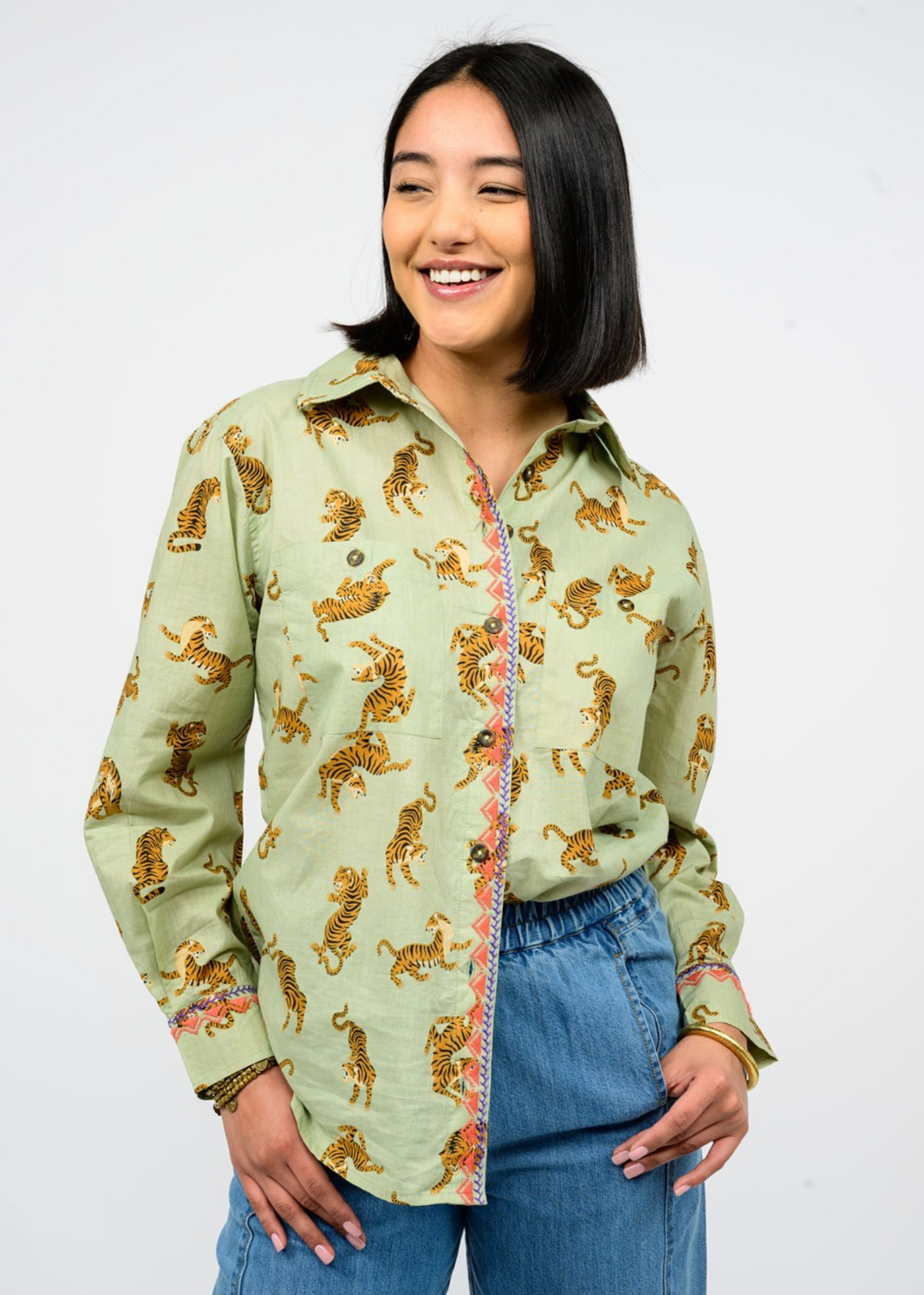 Woman wearing a sage green button down shirt with a tiger print and a collared neckline