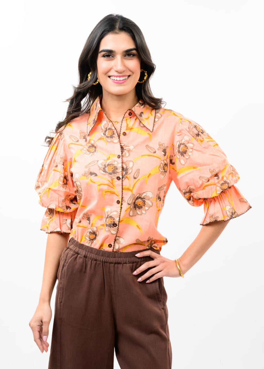 Woman wearing a coral floral button down top with puff sleeves and brown pants