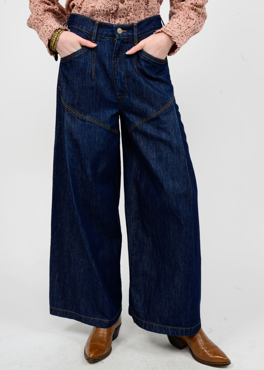 Woman wearing dark blue wide leg jeans with brown boots in front of a white background
