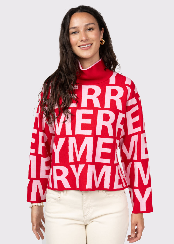 Woman wearing a red mock neck sweater with white "MERRY" letters and white jeans 