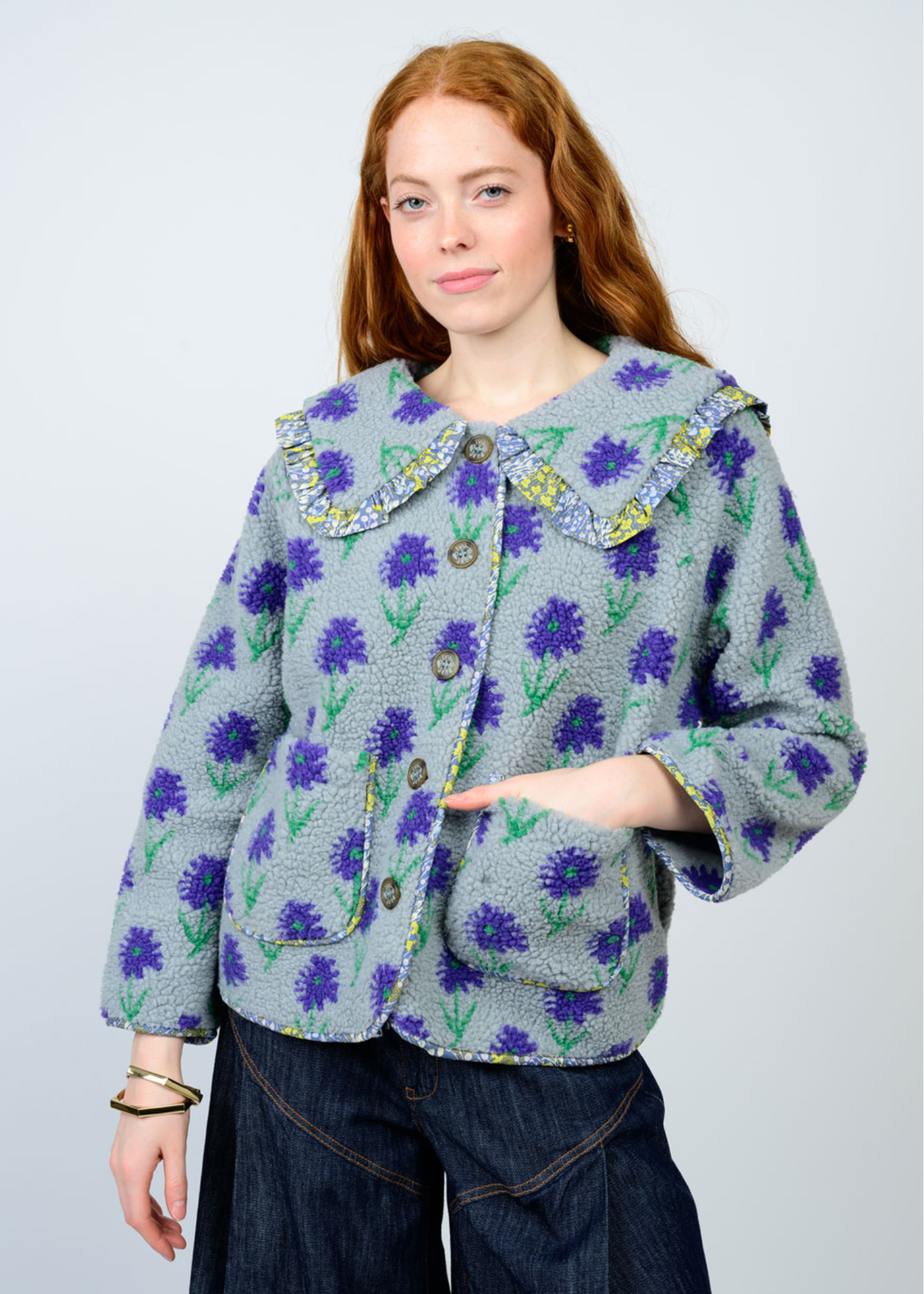 Woman with hand in pocket wearing a blue floral jacket against a white background