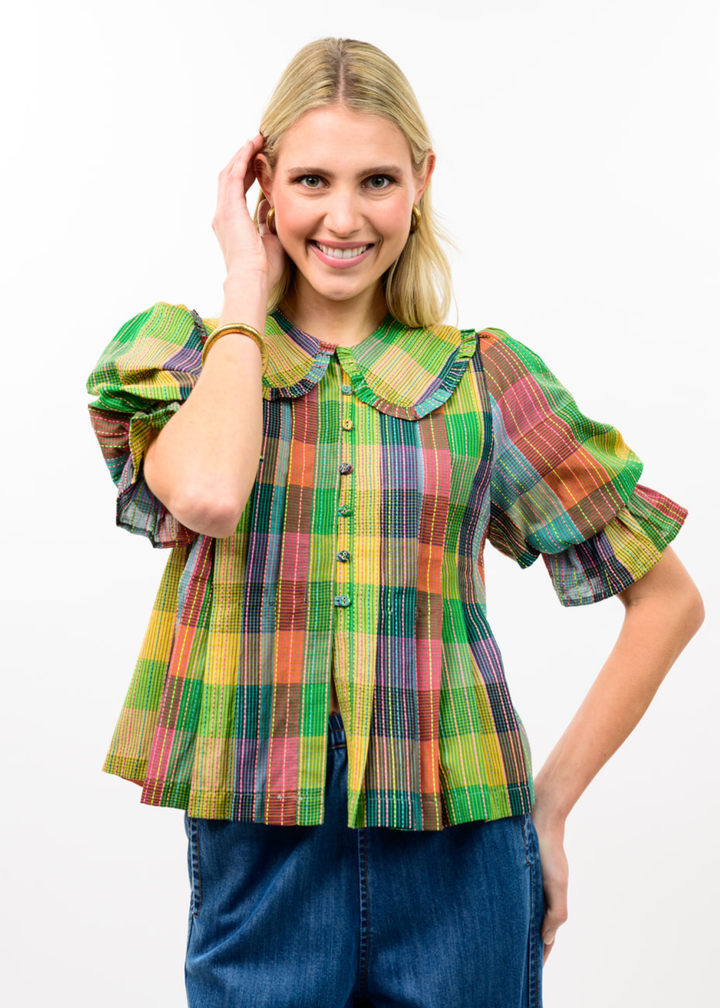 Woman wearing a multicolor plaid top with dark blue jeans against a white background