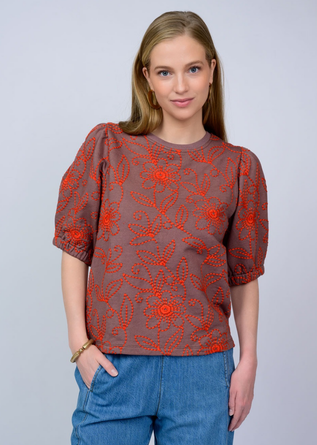 Woman wearing a brown top with red floral embroidery