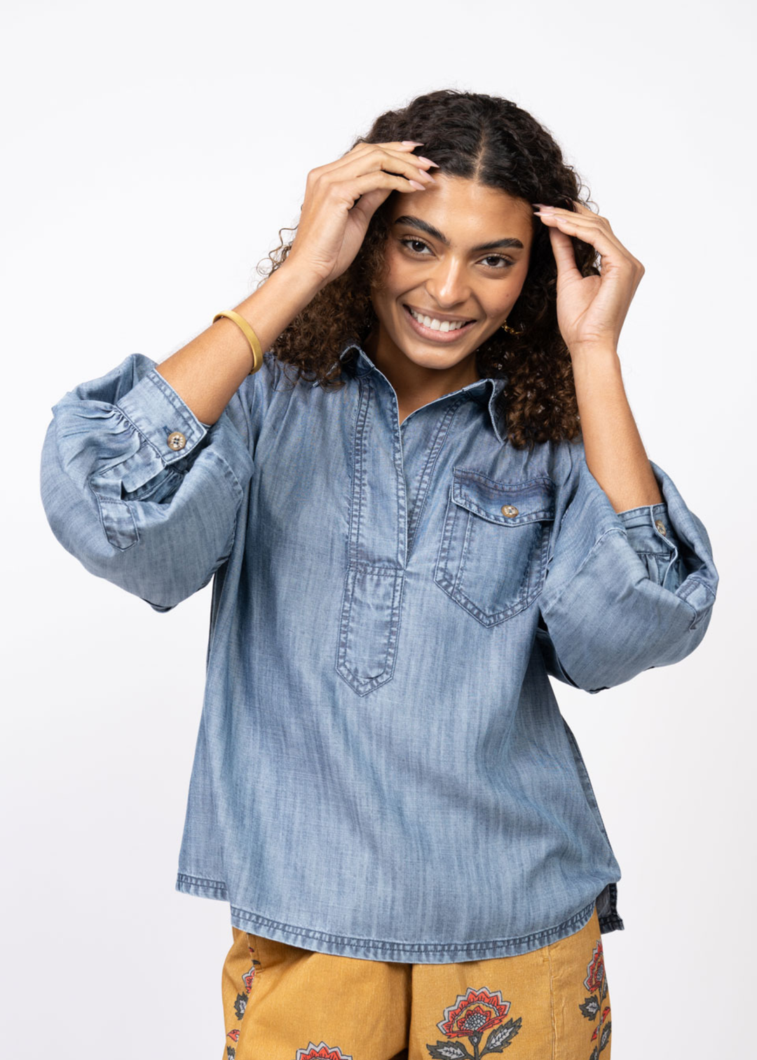 Woman wearing a denim collared shirt with yellow floral pants in front of a white background