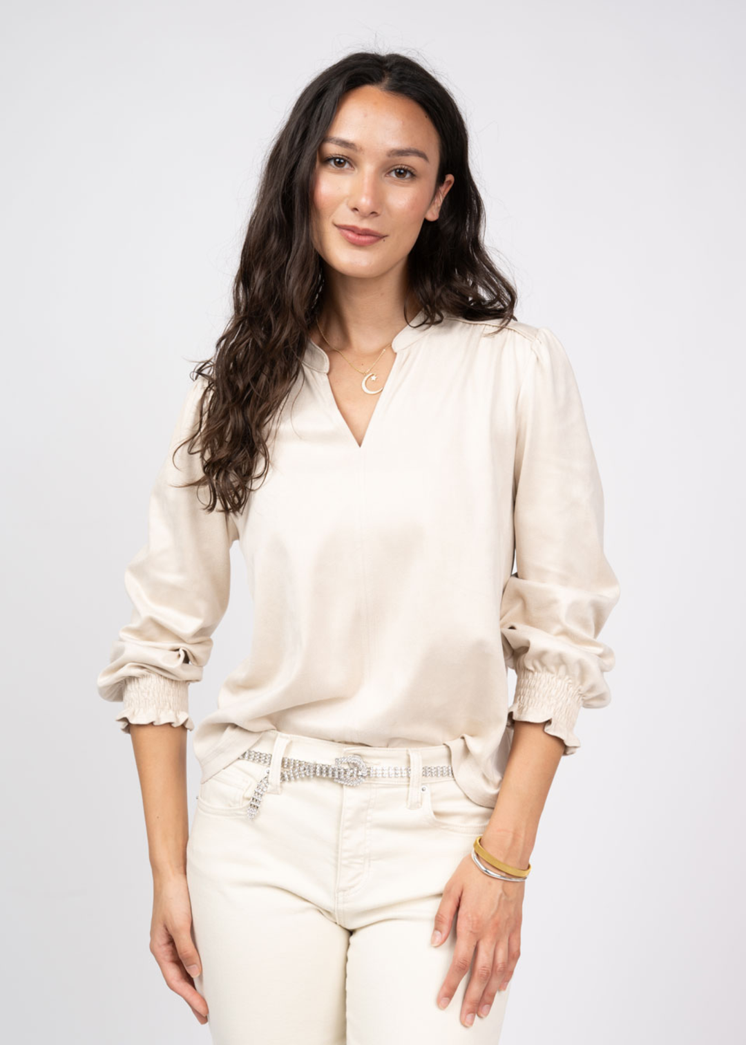 Woman wearing an ivory v-neck top with ivory jeans against a white background