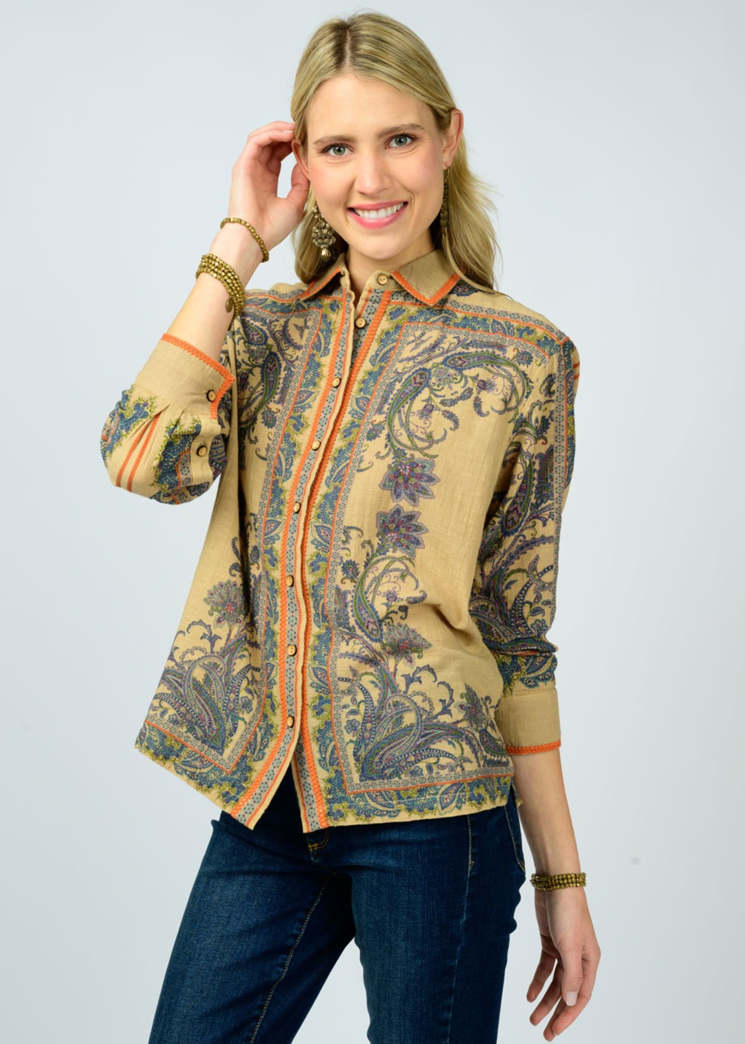 Woman wearing a camel colored button down top with a floral print with dark denim jeans against a white background
