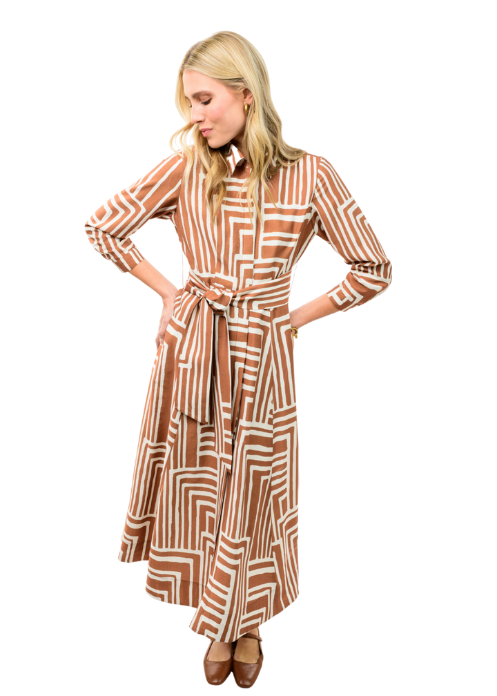 Woman wearing brown midi dress with collar and belt. It has white square patterns on it. 