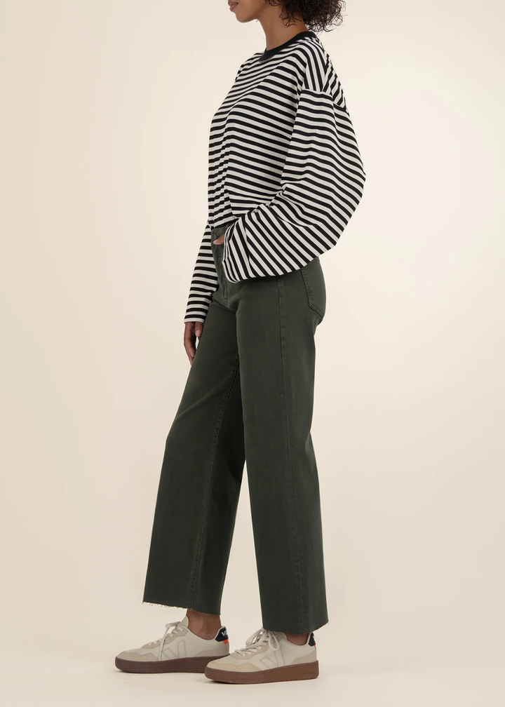Woman turned to the side wearing dark green jeans with a black and white striped sweater and white sneakers in front of a white background