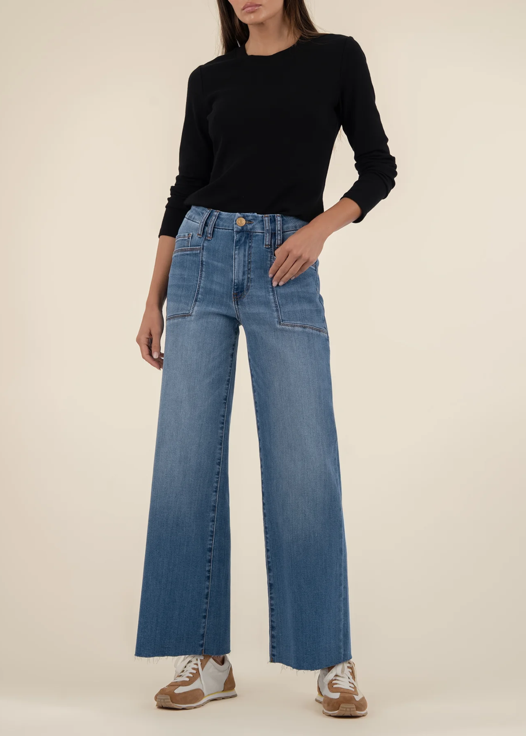 Woman wearing medium wash wide leg jeans with a long sleeve back top and brown and white sneakers