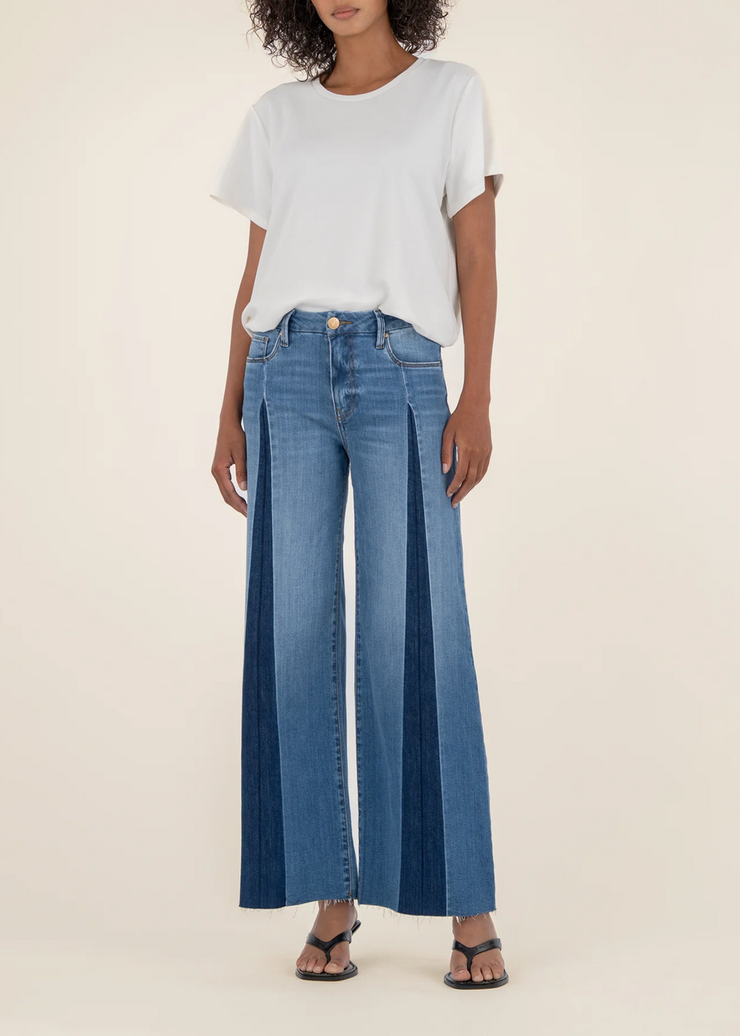 Woman wearing blue jeans with a dark blue front pleat in front of a white background
