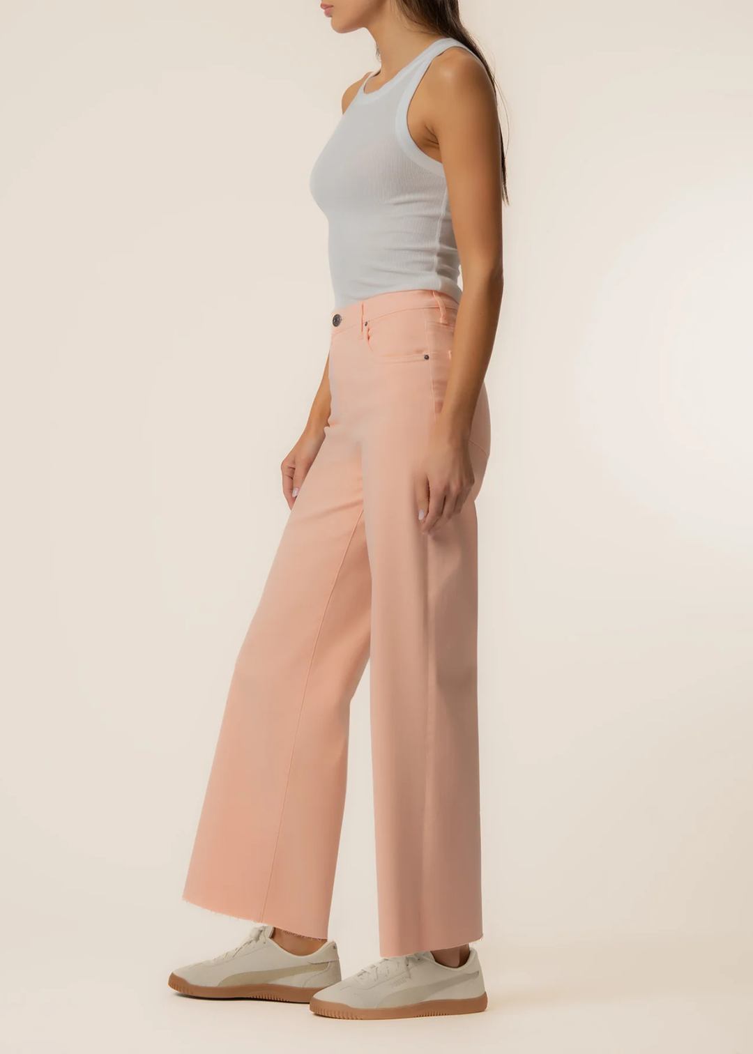Woman turned to the side wearing orange wide leg jeans with a grey tank and sneakers