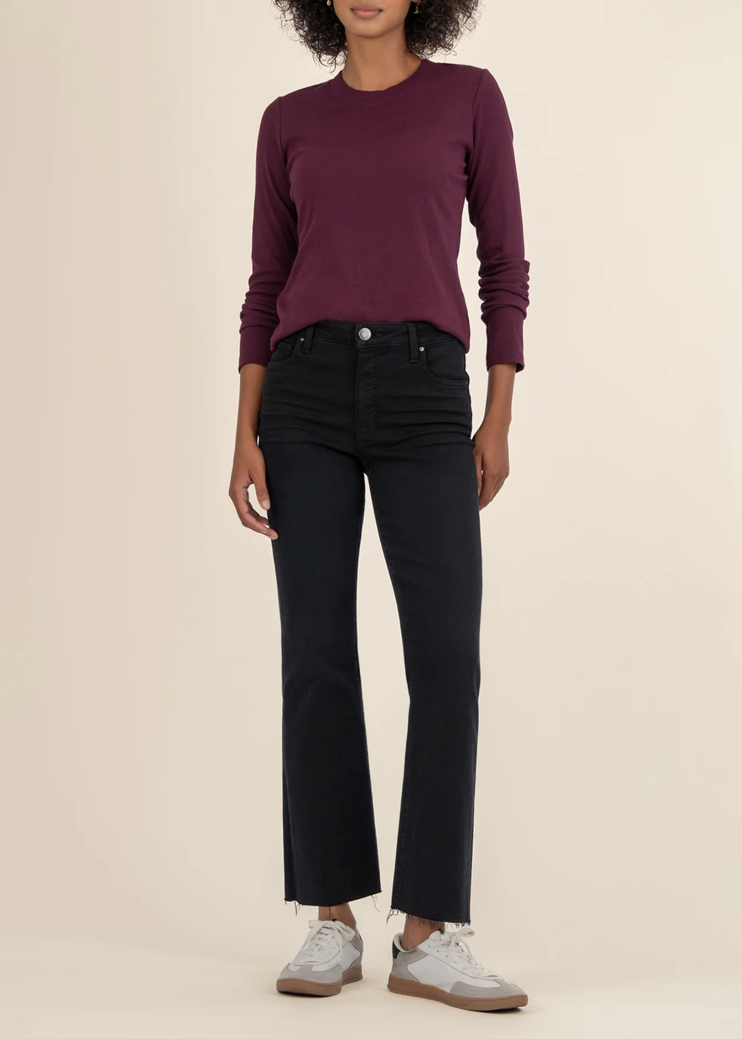Woman wearing a maroon long sleeve tee with black jeans and white sneakers in front of a white background
